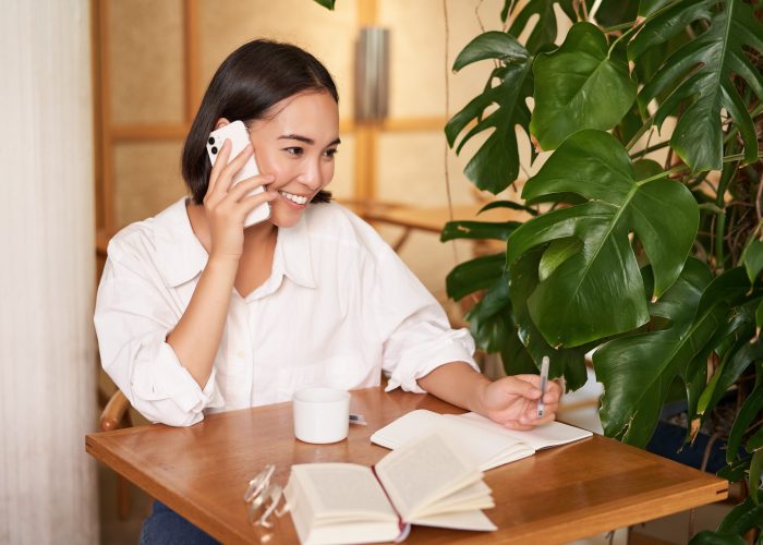 Working woman answer phone call in cafe, writing down, making notes while having conversation on telephone.